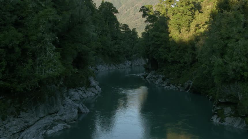 A river flows through a tree-lined gorge on a sunny day