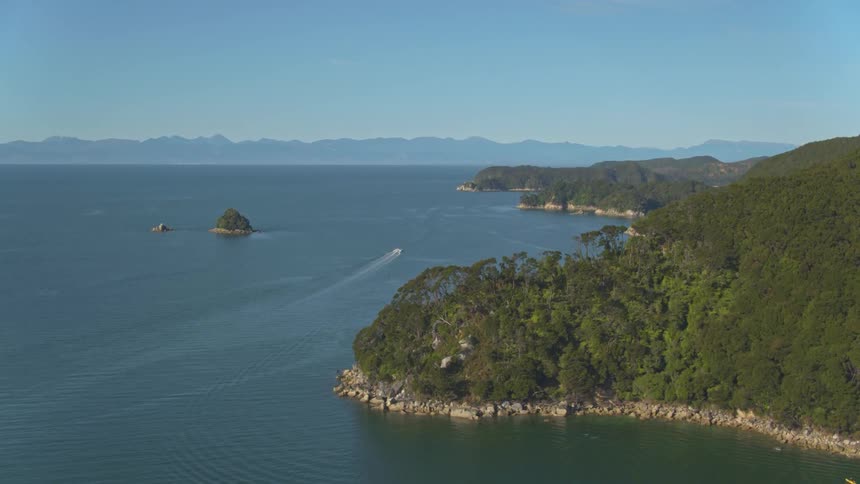 The boat is sailing past the island shore on a sunny day