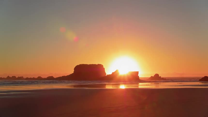 The sun is setting on the horizon beyond a rocky beach