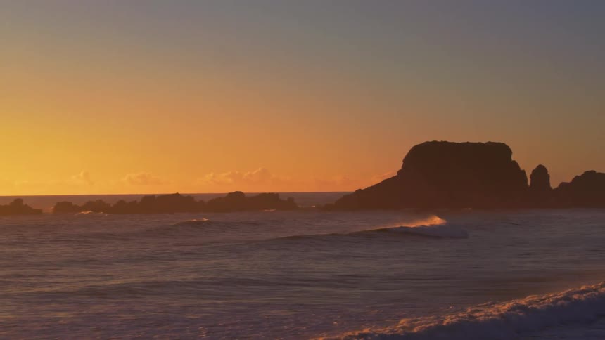 Waves come to shore past rock formations at sunset