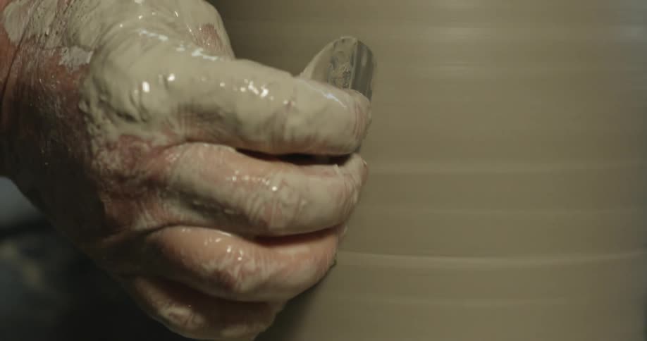 Hand holding a tool and shaping clay as it spins
