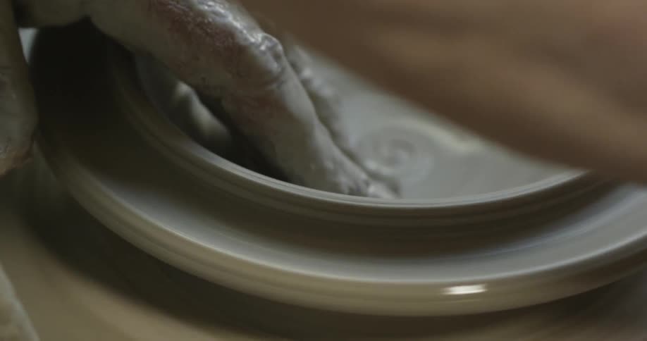 Hands working a wet clay vessel