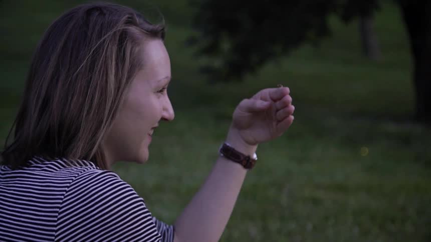Woman smiles while holding a firefly on her hand