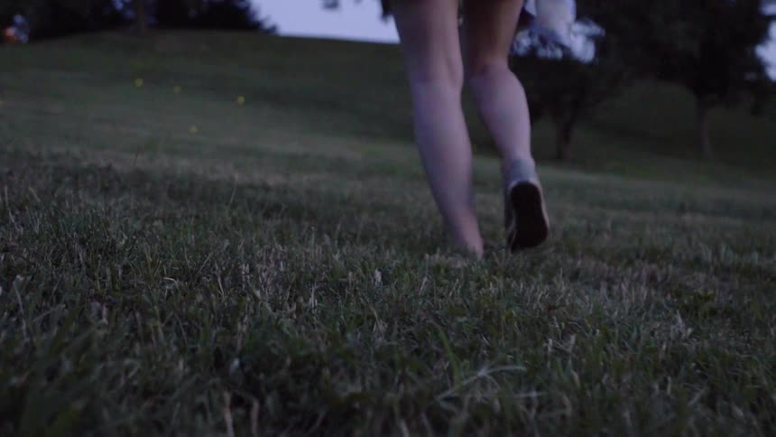 Fireflies glow in a park a woman is walking in at dusk