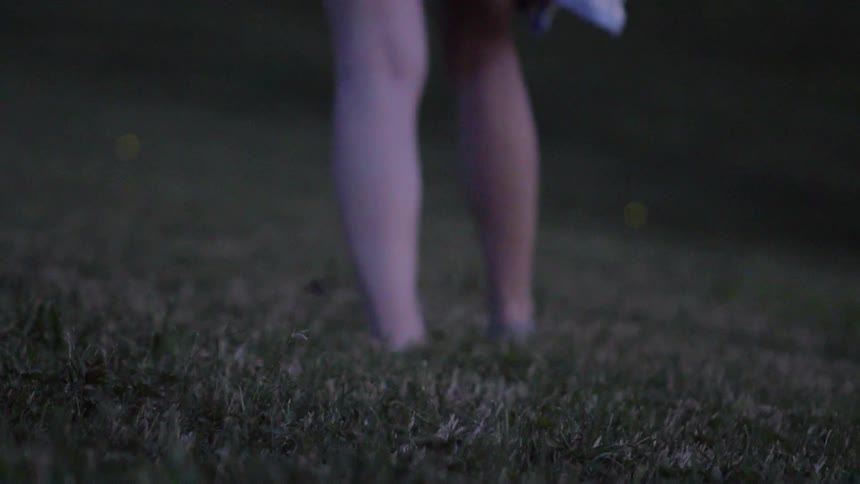 Woman walks through a grassy field with glowing fireflies
