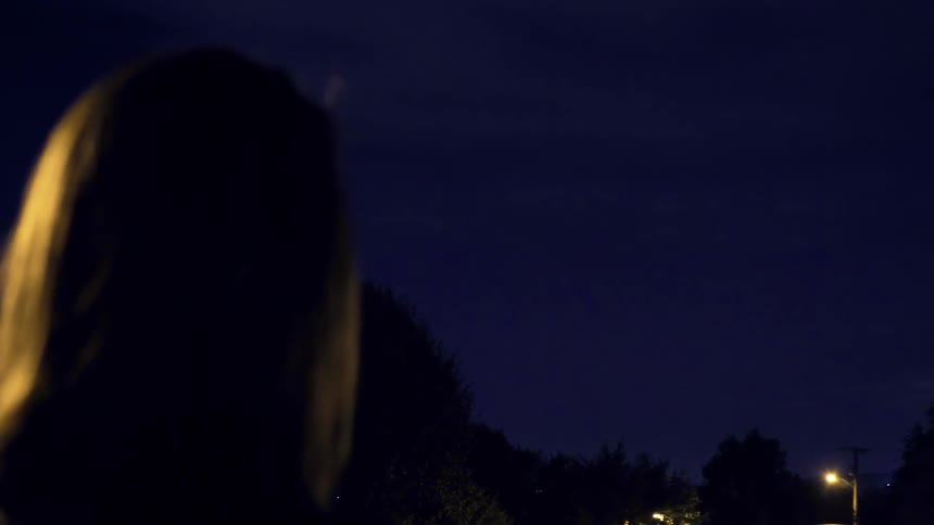 A woman watches the lightning over the trees