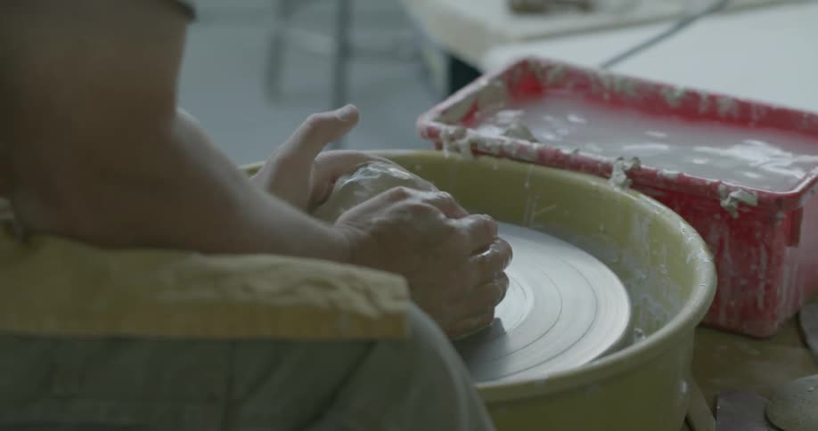 A person shapes clay to form a new object on a pottery wheel