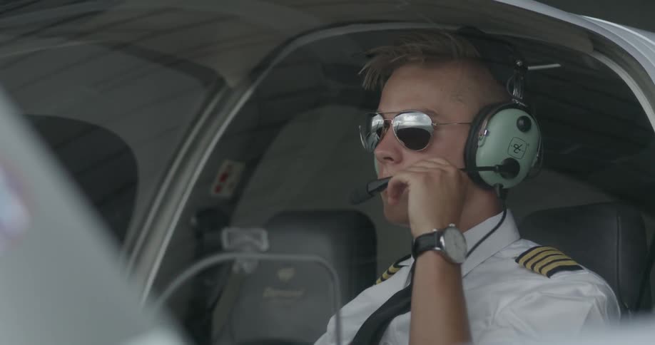 A pilot puts on his aviation headphones in a cockpit