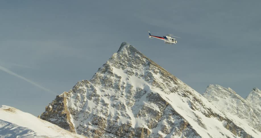 A helicopter flies over snowy mountains