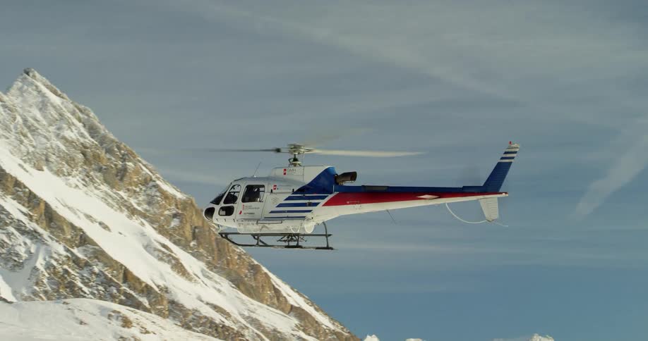 Helicopter flying close to snow-covered mountains on a cloudy day