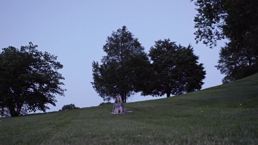 Woman sits on a blanket under a tree