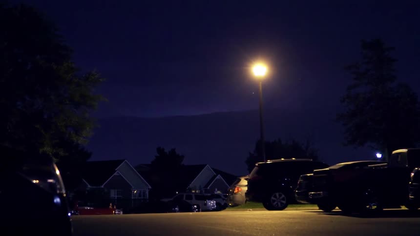Lightning is flashing over a quiet neighborhood at night