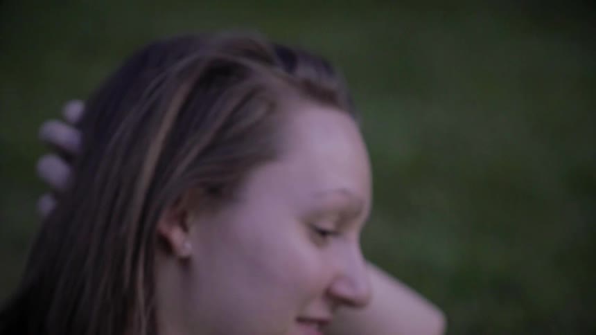 A woman sitting in a park at dusk is smiling and brushing back her hair