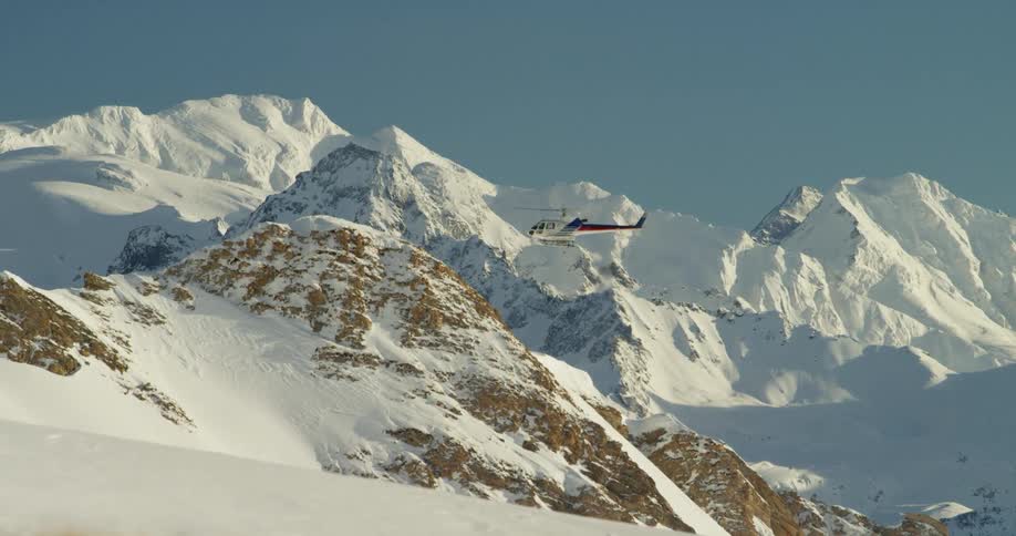 A helicopter is hovering above a snow covered mountain slope on a sunny day