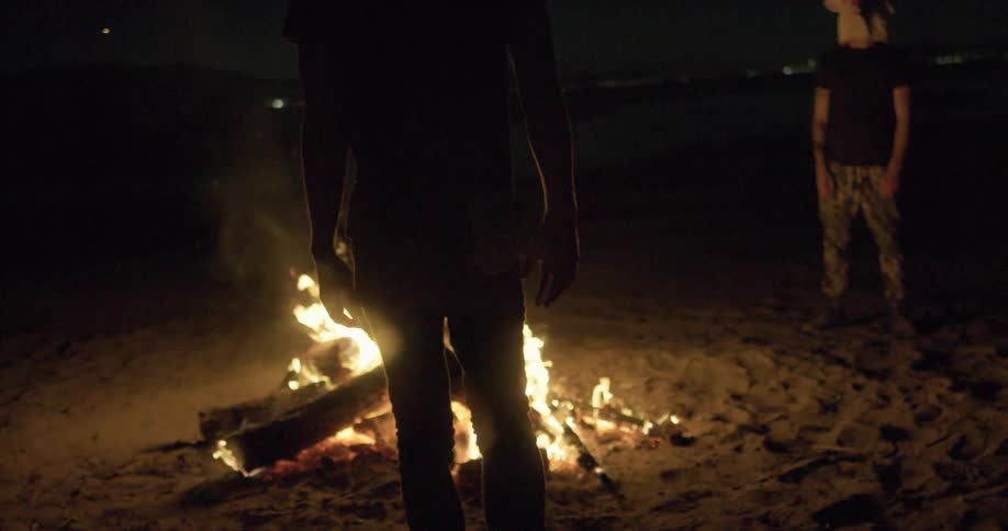People wearing animal masks stand outside by a fire