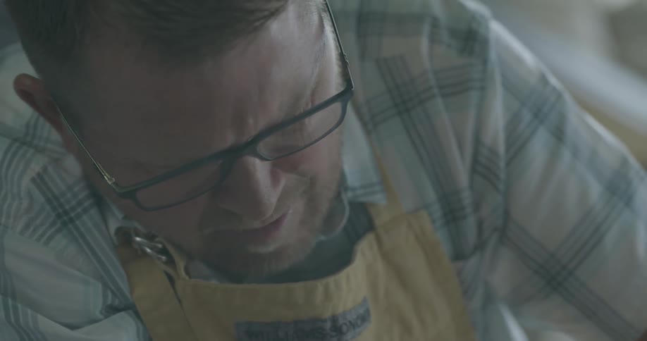 A man wearing an apron looks down at something he's working on