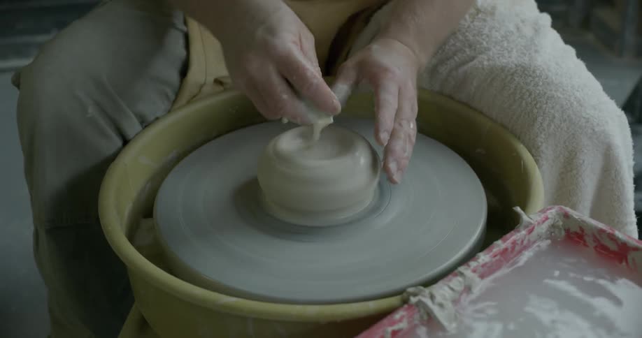 A man is forming a vase with some clay on a pottery wheel