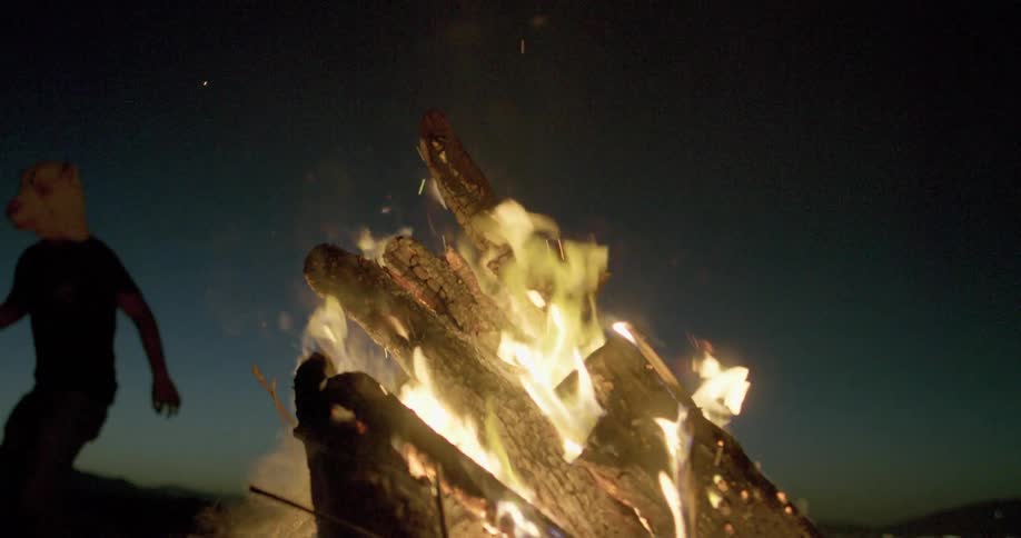 Men in sheep masks dance by a bonfire