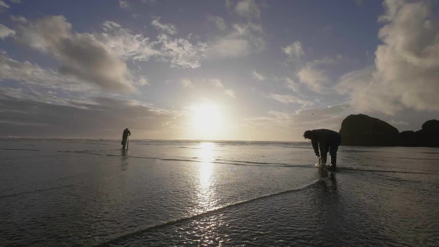 A couple of men are standing on the beach at high tide digging holes in the sand
