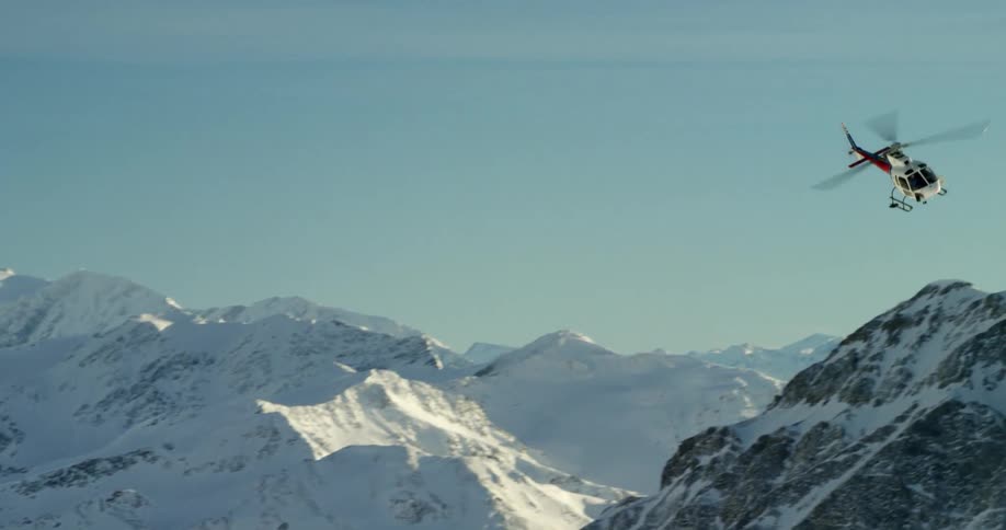 A helicopter flies over snowy mountains