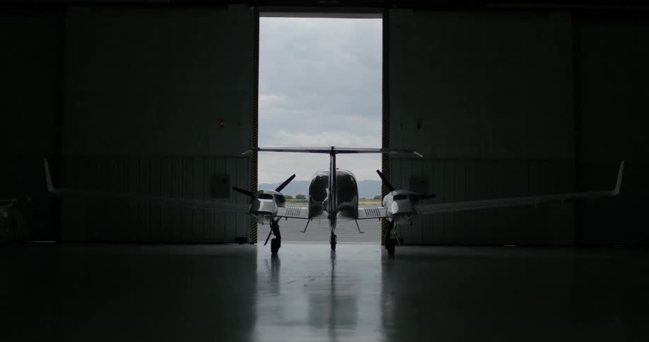 A large hangar door is opening to let a plane out