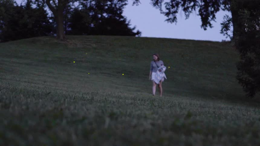A woman is walking through a field of fireflies