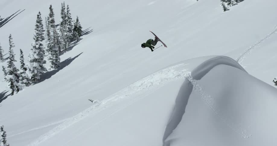 A skier does a flip as he goes down a slope during the day