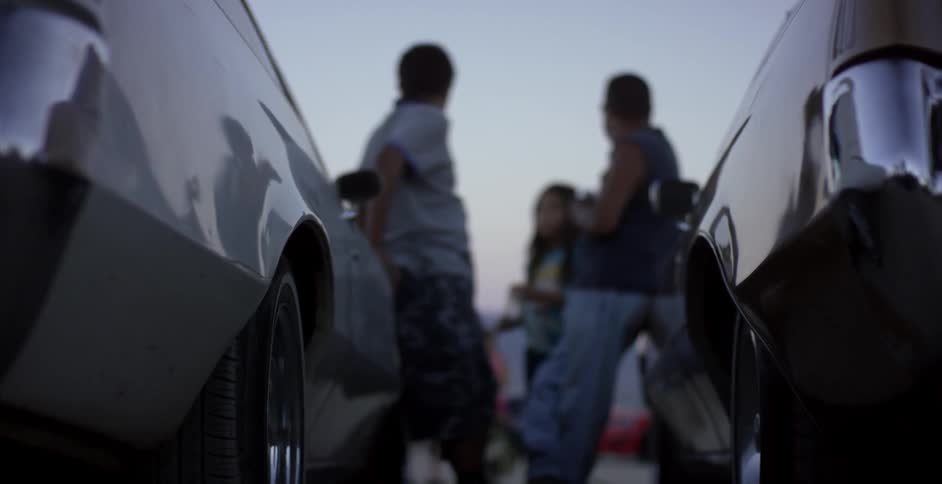People chat while leaned against cars