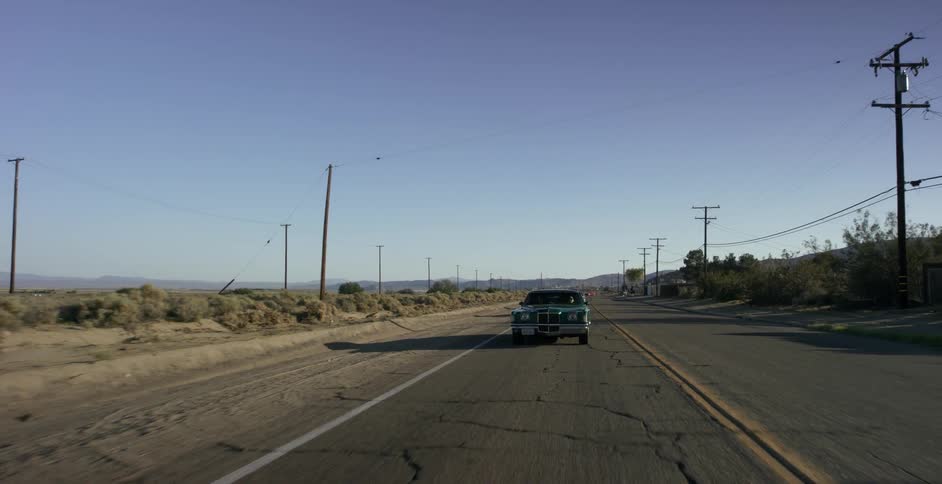A late model american car is driving on a desert highway during the day