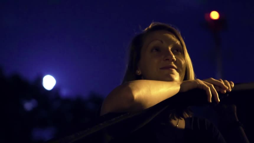 A woman is leaning against a car door looking at something and smiling