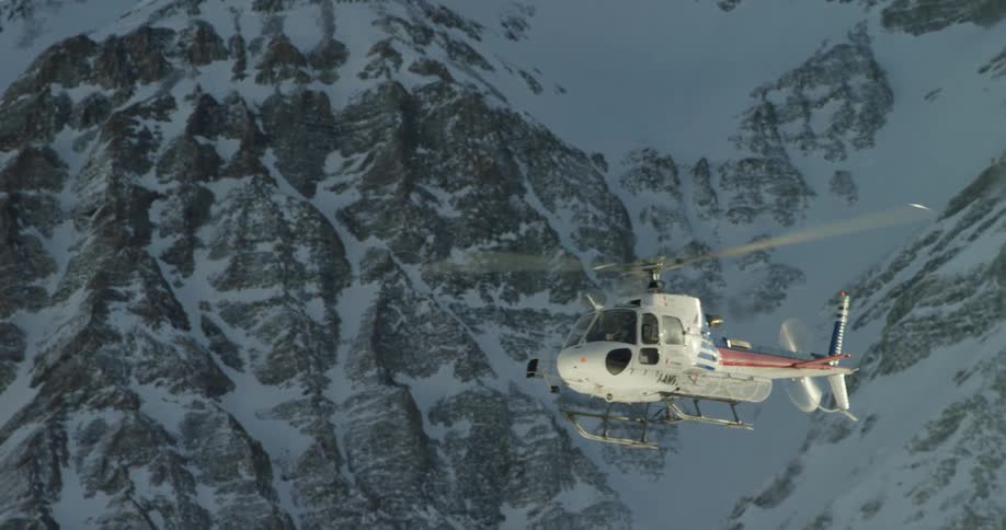 A helicopter flies past snow covered mountains