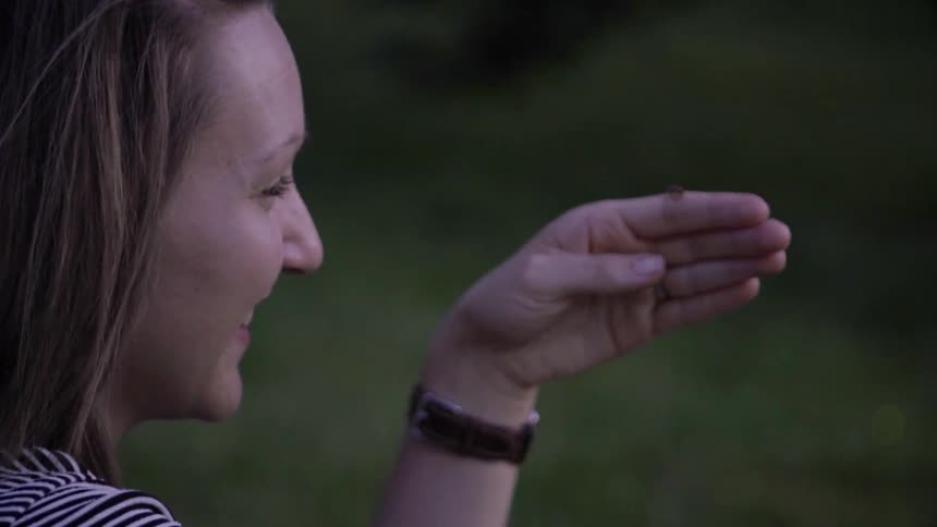 Woman smiles at firefly glowing on her finger