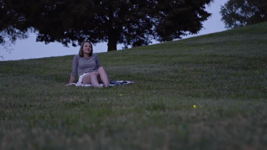 A woman lays in a field as fireflies flicker