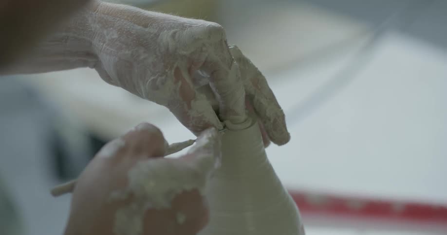 An artisan is sculpting a clay vase on pottery wheel