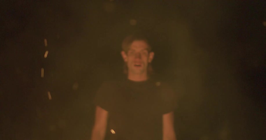 A man stands in front of a burning fire at night