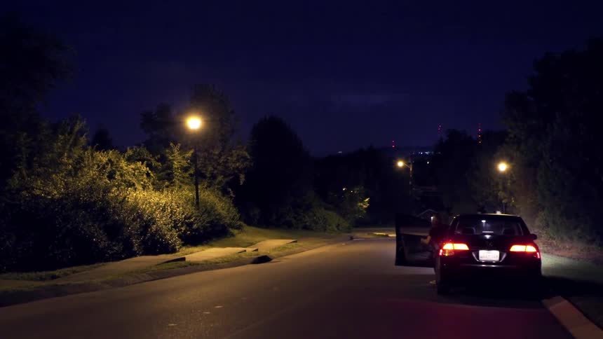 A car is parked on the side of the road watching lightning in the distance