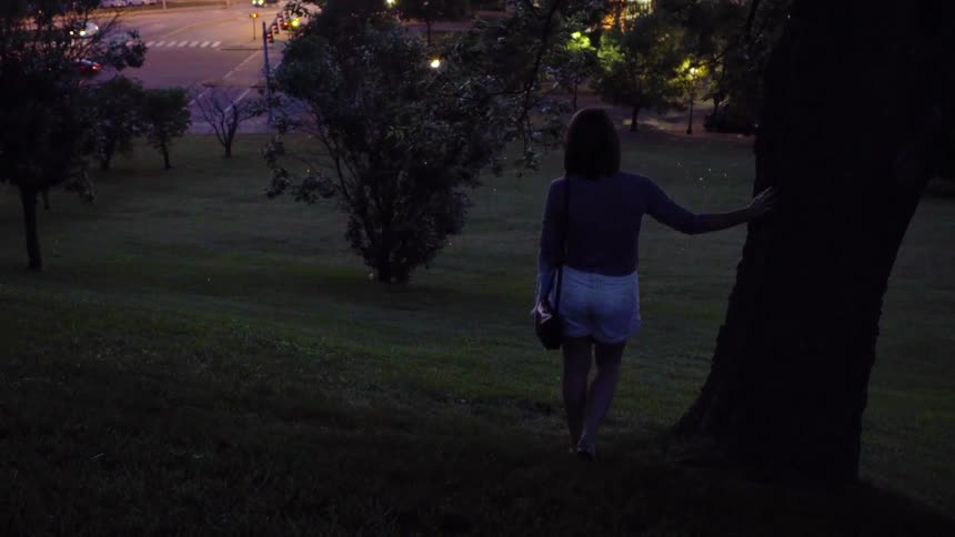 Woman walks outside and leans against tree trunk