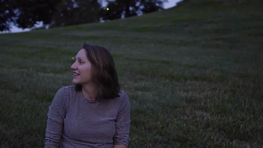 A woman smiles as she watches fireflies glow in a park at dusk