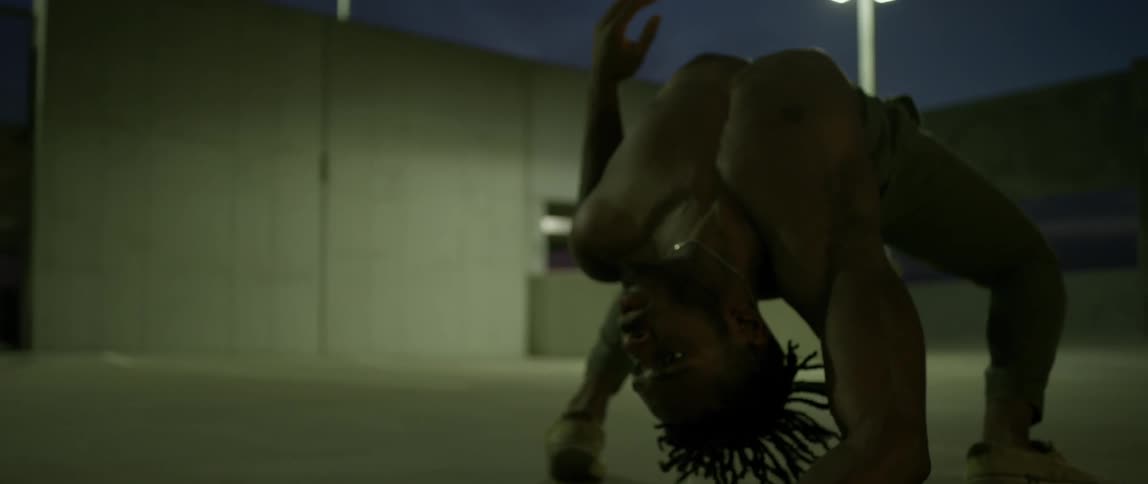 A man bends and arches his back as he dances on a garage roof at night