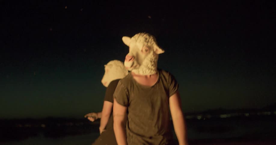Men in sheep masks dance around a fire at night