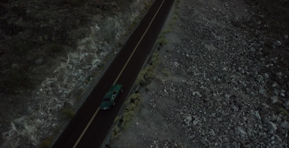 A late model american car is driving on a desert highway at night