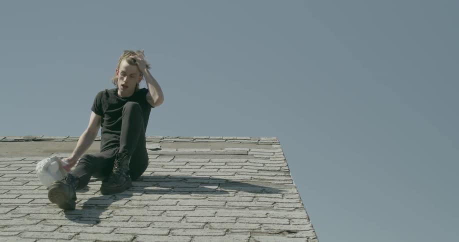 A man wearing a sheep mask sits up while on top of a roof