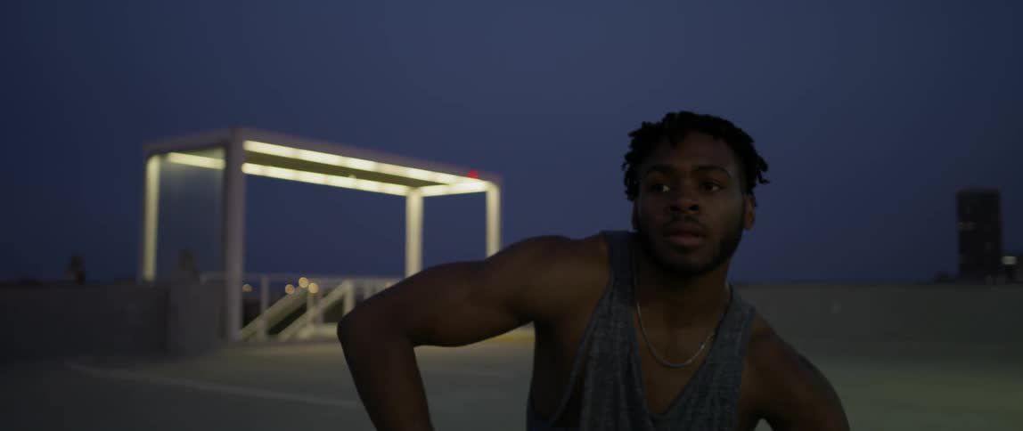 A man in a tank top of dancing on top of a parking garage