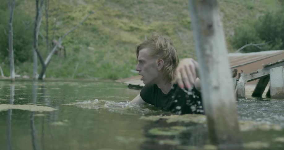 A man is wading in a swamp with flooded out old buildings during the day