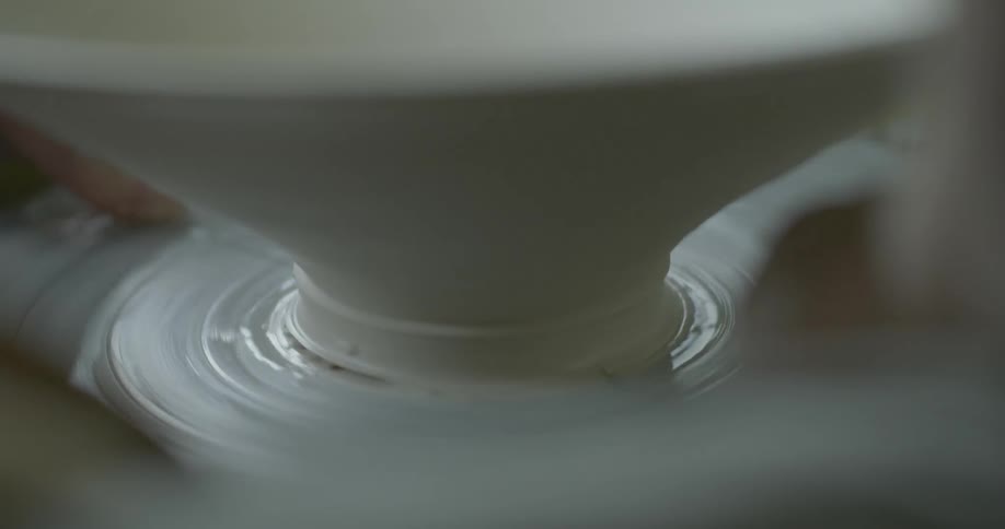 Someone is cutting clay with a piece of wire on a pottery wheel