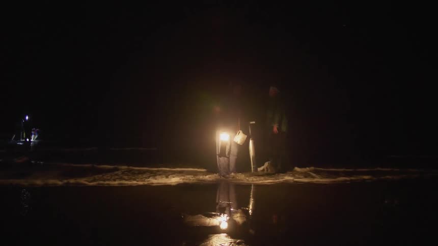 Men with lanterns wade in the surf to do some clam digging