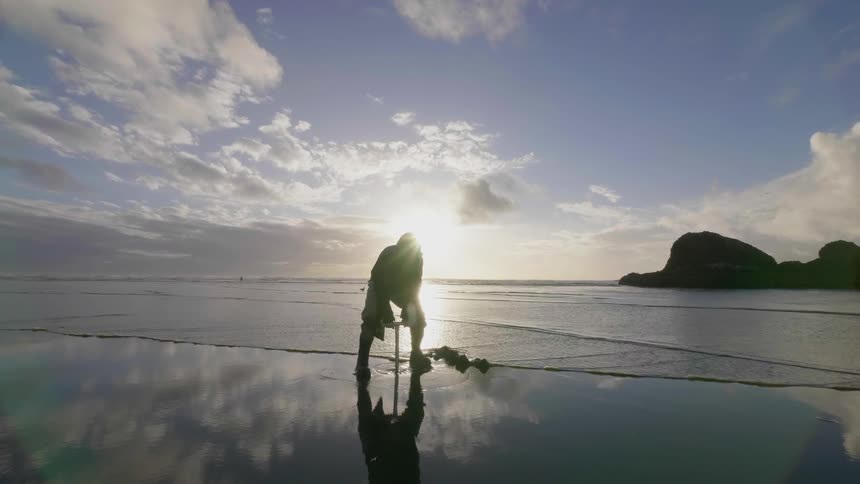 A person uses a clam digger to pull up sand on a beach