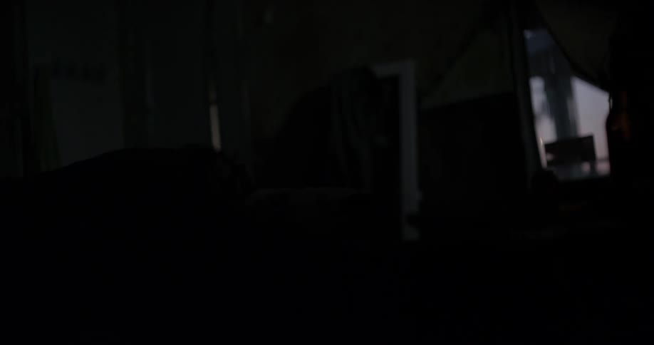 Man sleeps in a dark room while someone walks by