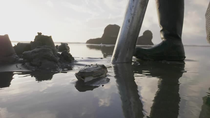 A person stands in watery mud holding a mesh bag