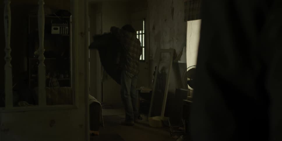 Man walks through a dim room and puts on his coat